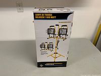 Front view of the boxed 1000 watt halogen work light showing dual lamps mounted on adjustable tripod stand.