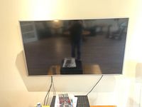 Front view of wall-mounted Vizio 65-inch LED TV with remote and manuals on table