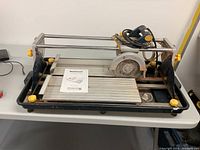 Full view of Mastercraft wet tile saw on table showing rails, cutting surface, motor, water tray, and owner's manual.