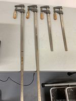 Four metal bar clamps laid out on a table with two long clamps measuring 36 inches and two shorter clamps measuring 18 inches.