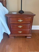 Front view of one bedside table showing three drawers and brass pulls