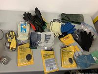 Photo showing an assortment of gloves including packaged Firm Grip coated gloves, leather gloves, cotton and rubber gloves laid out on a table