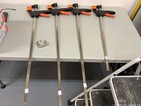 Four bar clamps laid out on a table, three long and one shorter, with an adjacent tape measure for scale.