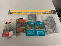 Top-down image of seven drill bit sets arranged horizontally with one long yellow Irwin drill bit package on top.