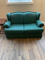 Front view of the green fabric love seat sofa showing two cushions, wingback design, and rolled arms.