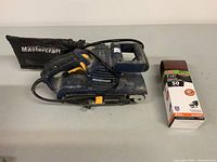 Mastercraft belt sander with dust collection bag and extra sanding belts in box, side view