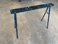 Single assembled sawhorse showing blue steel frame, black plastic top and foldable legs