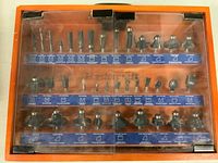 Top view of closed orange case showing 3 rows of router bits behind clear plastic doors, with blue labels indicating bit types and profiles.