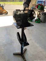Front angle view of Maximum 6-inch bench grinder mounted on metal stand with foot pedal in indoor garage setting.