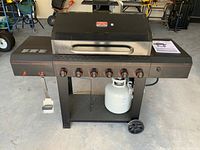 Front view of grill showing six control knobs, hood, side shelves and mounted propane tank