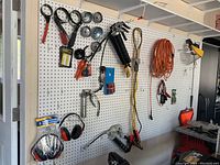 Full view of the pegboard with various tools and accessories arranged on hooks including oil filter wrenches, grease guns, hand tools, and extension cord.