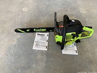 Side view of chainsaw laid on concrete next to printed manuals