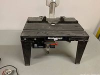 Front view of the Mastercraft router table showing ribbed plastic surface, power switch with red safety cover, and legs.