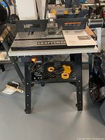 Full front view of router table on stand showing tabletop, fence, owner’s manual and accessories on lower shelf