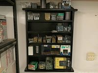 Full view of black wall shelf with multiple rows of various screws and hardware in plastic containers and boxes.