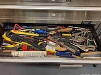 Full view of drawer filled with assorted hand tools including pipe wrenches, clamps, wire brushes, crowbars, saws, and pliers.
