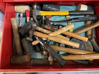 Top view of a red shelf drawer containing a collection of hammers and mallets of various types and handles.