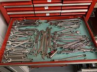 Top-down view of open and box-end combination wrenches arranged on green felt inside a red tool chest drawer.