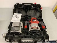 Top-down view of router in molded black plastic carry case with instruction manual beside it.