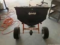 Front view of black hopper mounted on orange frame, showing Agri-Fab logo and pneumatic tires