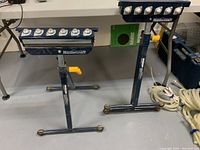 Two Mastercraft adjustable height workpiece support stands with ball transfer rollers on top, dark blue steel frame, yellow adjustment lever, showing overall view and condition.