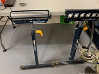 Front view of both Mastercraft workpiece support stands placed side by side, showing the adjustable height metal rollers and yellow locking levers.