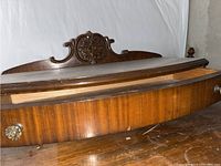 Close-up of the top back panel with ornate carved wood detail and part of the drawer top with a visible wooden knob.