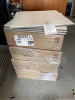 Four stacked boxes of Daltile white 12x12 ceramic tiles with four loose tiles placed on top. Boxes show product labels with size and brand information.