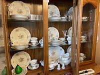 Full view of china set and assorted glassware displayed in wooden hutch with glass doors.