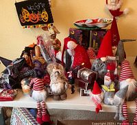 Wide view of assorted Christmas and Halloween figurines and decorations displayed on a shelf including several plush Santas, gnomes, and ornaments.