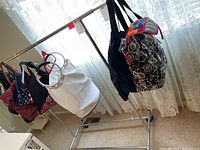 Photo showing chrome metal clothes rack with multiple bags hanging as a demonstration; rack itself is the item for sale, measuring approximately 48 x 22 x 37 inches.
