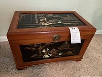 Full view of the wooden jewelry chest with lacquered front and top panels showing Japanese style scenes and brass clasp lock on front.