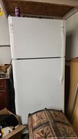Full front view of white Kenmore refrigerator with top freezer. Shows some surrounding garage items and indicates unit size and condition.