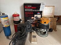 Wide view of all items on table including Rosette Maker box, router, two sanders, propane tanks, torch, and manual.