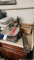 Front side view of Craftsman scroll saw on workbench with boxes of blades and accessories nearby.