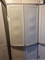 Front view of a tall plastic storage cabinet with two louvered doors, showing its size and door design.