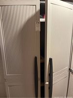 Front side angle showing two-door plastic storage cabinet with vertical ribbed design and black handles.