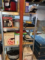 Kitchen appliances and miscellaneous items on metal shelving including boxed and unpackaged items.
