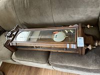 Full side view of the German wooden wall clock showing glass front and brass pendulum inside the case.