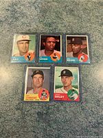 Five 1963 Topps baseball cards laid out in plastic sleeves on green surface, showing players Joe Jay, Ted Savage, Al Wilson, Bob Studivant, and Purnal Goldy.