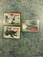 Three 1965 war cards laid out on a surface showing various scenes with red labels.
