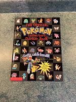 Front cover of the Pokémon collectors sticker book showing the title and many original Pokémon characters in a grid pattern on a black background.
