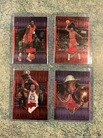 Four Michael Jordan basketball cards laid out on carpet, protected in plastic sleeves. Cards feature dynamic action shots and text highlighting key achievements.
