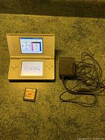 White Nintendo DS open showing Sudoku game on top and bottom screens, with charger and game cartridge placed beside it.