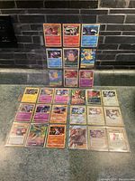 Photo showing a collection of 28 Pokémon trading cards in protective sleeves arranged in pages on a counter. Cards include holographic and standard types.