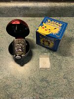 Gold plated Pikachu bar inside open Poké Ball case, original Pokémon box nearby, certificate of authenticity in front