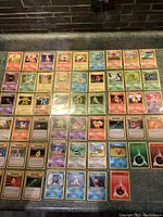 Photo showing a page of Pokémon cards arranged in protective sleeves including various Fire, Psychic, and Grass type Pokémon with Trainer cards below.