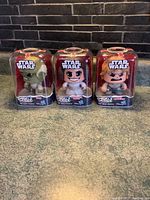 Three Star Wars Mighty Muggs figures in packaging displayed on a surface against a brick background.