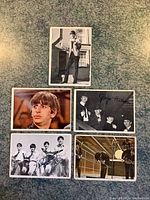 Six vintage Beatles collectible cards laid out on a greenish surface showing individual and group photos, some signed