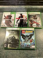 Photo of front cover art for all 5 Xbox 360 games, showing titles Prototype 2, Just Cause 2, Splinter Cell Conviction, Fallout 3, and LEGO Batman.